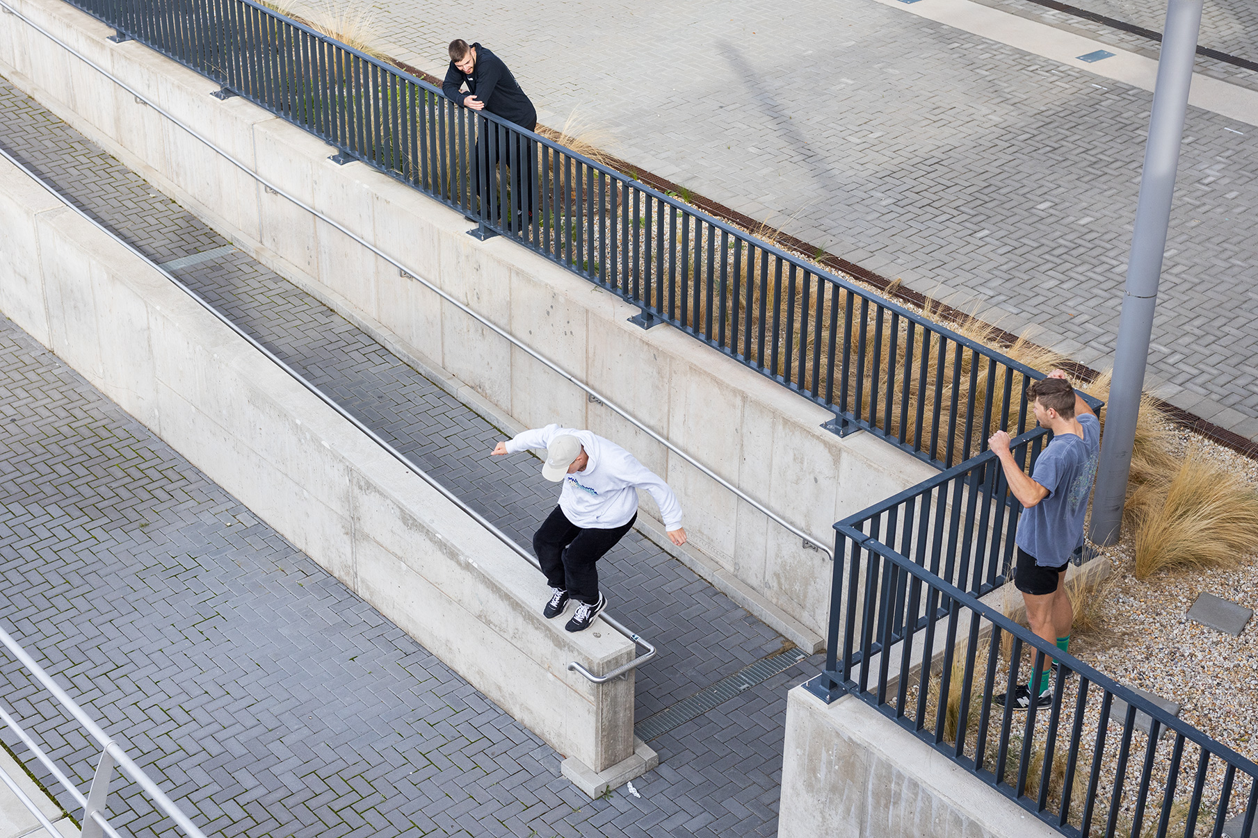 Drei Personen trainieren Parkour im Outdoor-Bereich – zwei schauen zu wie eine dritte Person auf eine Mauer springt.